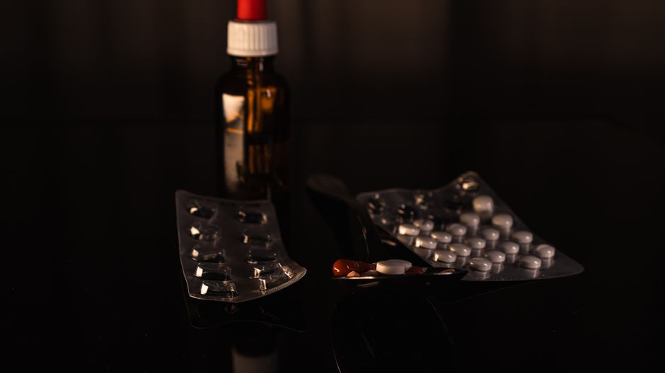 A collection of pharmaceuticals including pills and a bottle on a dark surface.